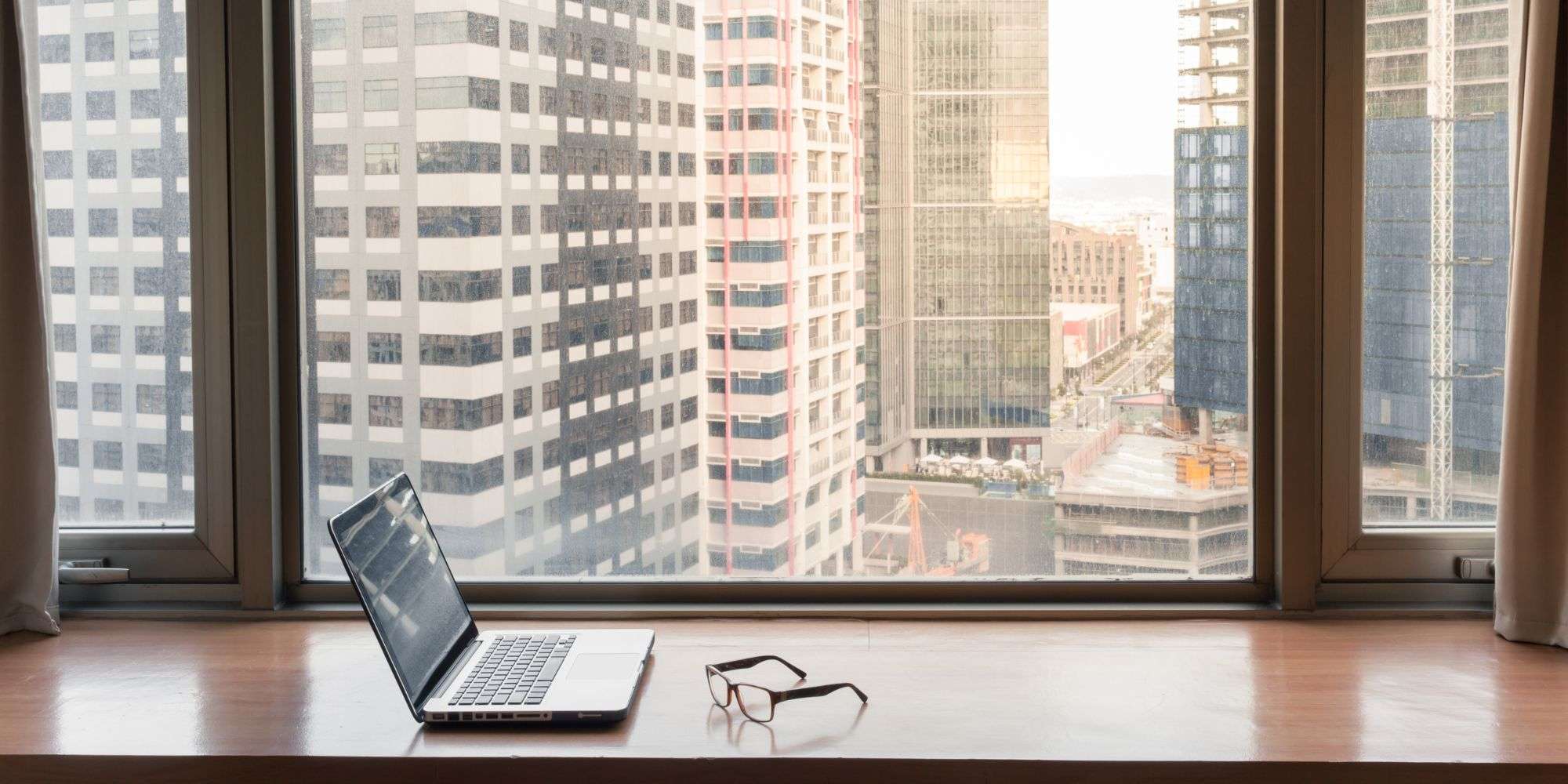 Laptop and glasses on a windowsill overlooking urban skyscrapers, symbolizing remote work and organizational change.